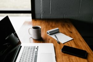 A tidy desk with an open laptop, a planning notebook, and a coffee cup — a calm, organized workspace for building an AI system from experiments into operations.